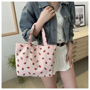 Pink corduroy tote bag with strawberry print being held by a model in a cozy room