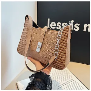 Macro view of beige crocodile embossed leather bag with silver chain and metal buckle