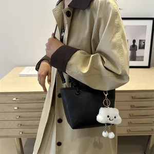 Black pebbled leather bucket bag with a cute plush cloud charm shown in a cozy home setting