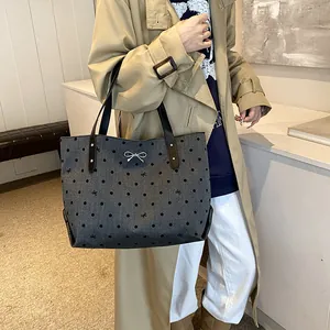 Large gray polka dot tote bag with metal bow detail, styled with a beige trench coat