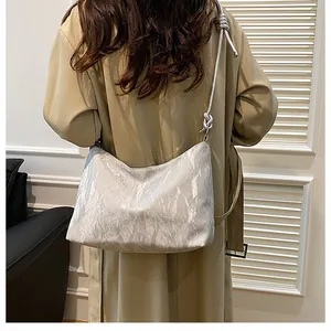 Silver metallic crinkle shoulder bag featuring elegant knotted strap detail on a model