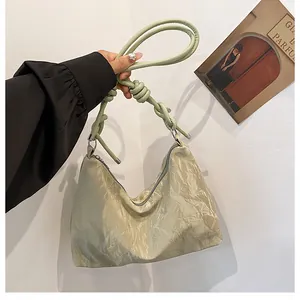 Close-up of light green pleated shoulder bag with unique knotted strap and metal buckles