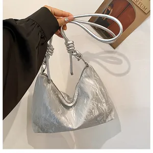 Detail of silver metallic handbag featuring creative knot strap and pleated texture