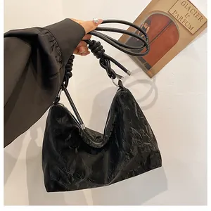 Detail of black pleated shoulder bag with knotted strap and silver metallic hardware