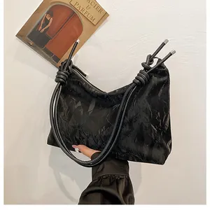 Detail of black tote bag featuring textured crinkle material and stylish knotted strap
