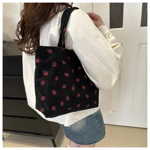 Detail of black corduroy tote bag featuring red strawberry embroidery and soft texture