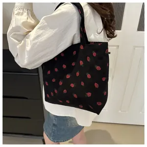 Close-up of black corduroy tote bag with red strawberry pattern and woven handle