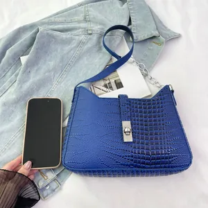Size comparison of a navy blue crocodile pattern underarm bag next to a smartphone