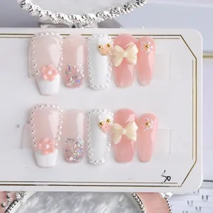 Detail of handmade press-on nails featuring pink floral relief, pearls, and bows
