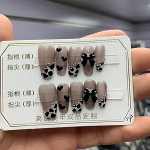 Macro shot of long coffin fake nails with cow prints, black bows, and rhinestones