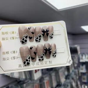 Detail of pink press-on nails featuring black bows, heart patterns, and pearls decor