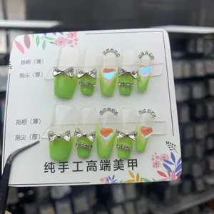 Detail of green gradient press-on nails with rhinestone bows and heart-shaped charms