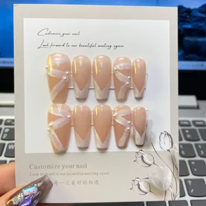 Detailed view of nude pink coffin press-on nails with white ribbon and pearl accents
