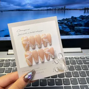 Detail of nude pink coffin press-on nails with white ribbons and pearl decorations