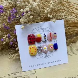 Artistic hand-painted press-on nails with colorful floral and glitter designs on display