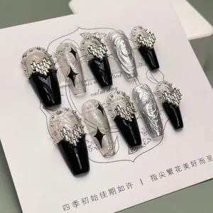 Macro detail of handmade black and silver press-on nails with 3D metal cross heart charms