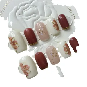 Faux ongles faits main ambre et rouge avec liseré doré et motifs floraux sur socle