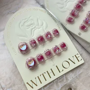 Pink glitter gradient press-on nails with heart charms and pearls on display card