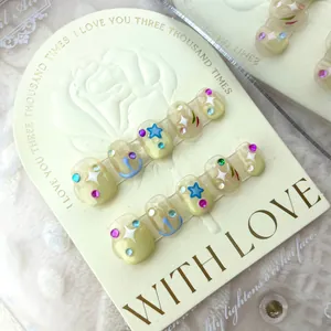 Short press-on nails featuring yellow base with stars, beads and blue abstract lines