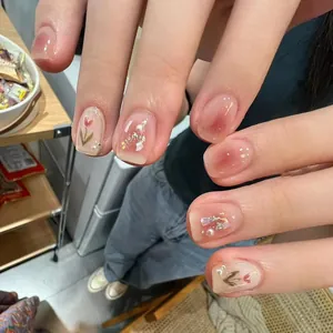 Close-up of pink press-on nails with hand-painted tulips, pearls and glitter accents