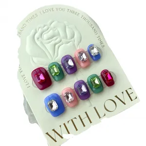 Handmade press-on nails with colorful rhinestones in deep red, green, and blue square shapes