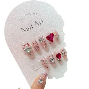 Sparkly raspberry red press-on nails with heart rhinestones and glitter on display card