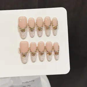 Faux ongles faits main dégradé rose nude avec décorations papillon dorées et strass