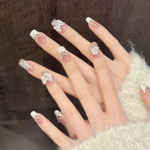 Close-up of handmade press-on nails with white 3D bows and pearls on a nude base