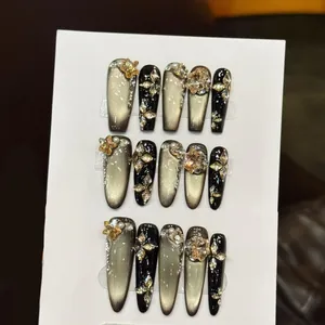 Detailansicht der schwarzen Katzenaugen-Kunstnägel mit goldenen Sternen und Perlen