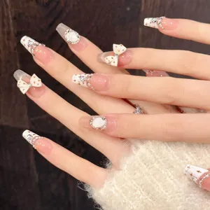 Detail of luxury press-on nails with white bows, pearls, and sparkling French tips