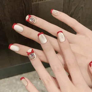 Détail de faux ongles rouges avec base œil-de-chat champagne et bijoux nœuds 3D
