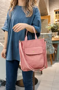 Pink corduroy tote bag with adjustable strap worn by a model in a cozy interior setting