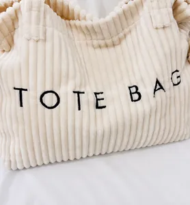 Detailed macro view of the cream corduroy tote bag with black letter embroidery