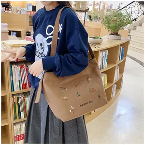 Close-up of brown corduroy tote bag with Harvest Day embroidery in a cozy bookstore setting