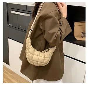 Side view of a beige quilted dumpling crossbody bag worn by a model in a modern kitchen