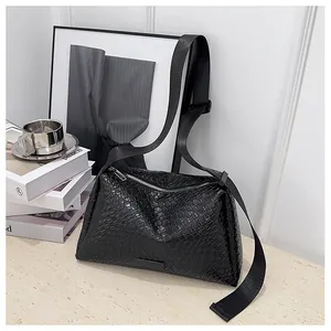 Gros plan sur la texture en cuir tressé noir et le zip argenté du sac à bandoulière