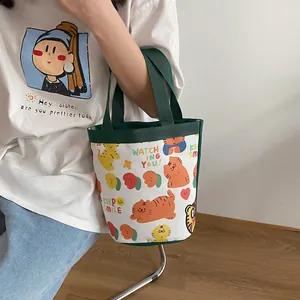 Detail of canvas bucket bag with green handles and cartoon tiger print shown by model