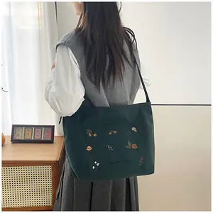 Macro detail of dark green corduroy tote bag featuring floral embroidery and Harvest Day text