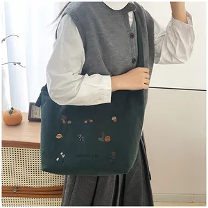 Close-up of green corduroy tote bag featuring Harvest Day embroidery and autumn patterns