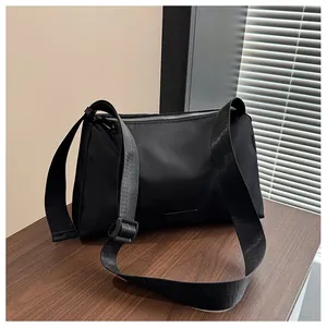 Détail du sac bandoulière noir avec sangle large posé sur une surface en bois