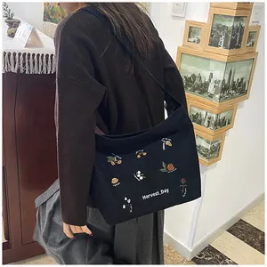 Detail of embroidered plant patterns and Harvest Day text on black corduroy tote bag