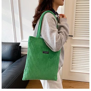 Dettaglio della borsa tote in velluto a coste verdi con etichetta FASHION sulla spalla