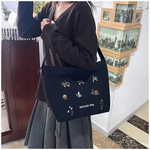 Detail of floral embroidery and Harvest Day text on black corduroy tote bag surface