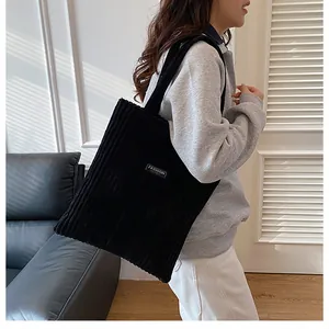 Dettaglio della borsa tote in velluto a coste nero con etichetta Fashion indossata a spalla