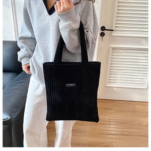 Dettaglio borsa tote in velluto a coste nero con etichetta fashion indossata da modella
