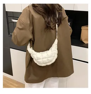 Quilted off-white crescent crossbody bag with adjustable strap worn by a model