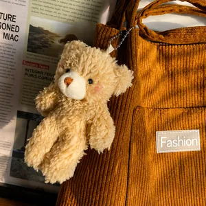 Close-up of cute light brown plush bear charm attached to a brown corduroy bag strap