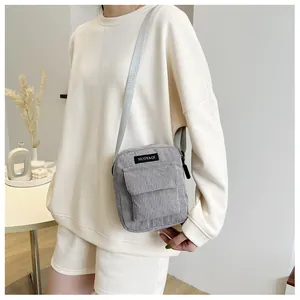 Detail of grey corduroy crossbody bag featuring adjustable strap and front flap pocket