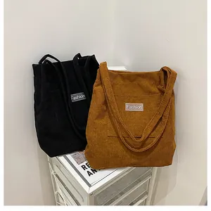 Detail of corduroy tote bags in black and tan with Fashion label on white trolley
