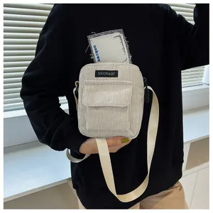 Close-up of a white corduroy crossbody bag with adjustable strap and brand tag